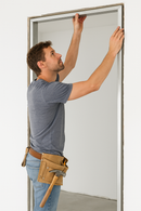 Male worker installing an aluminium door frame while adjusting the top section with his hands.