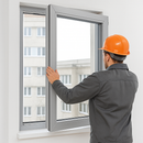 Worker in orange hard hat installing an aluminium window frame in a building wall.