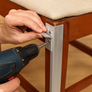Person installing aluminum corner bracket on wooden chair with drill
