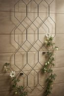Modern black wall trellis with white flowering vine on beige tile wall.