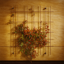 Rust-toned square metal trellis with climbing foliage on a golden wall.