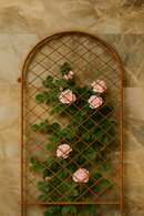 Rustic metal trellis with pink roses and green leaves against a marble-patterned wall.