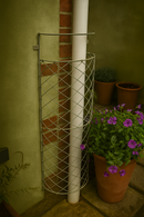 White drainpipe with metal trellis beside purple potted flowers.