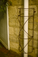 Rustic metal drainpipe trellis on stone wall with white pipe.
