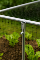 Close-up of an aluminum top rod fixed to a vertical corner post with black mesh netting, forming a sturdy vegetable cage frame in a garden.