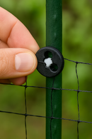 Hand securing netting to a green garden post using a round plastic fixing clip.