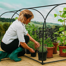 Woman gardening under open grower frame with potted herbs and veggies.