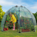 Woman gardening inside a transparent dome greenhouse on grass.