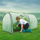 Woman tending plants inside mesh grow tunnel on green hillside.