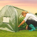 Woman gardening in mesh greenhouse at sunset on grassy field.